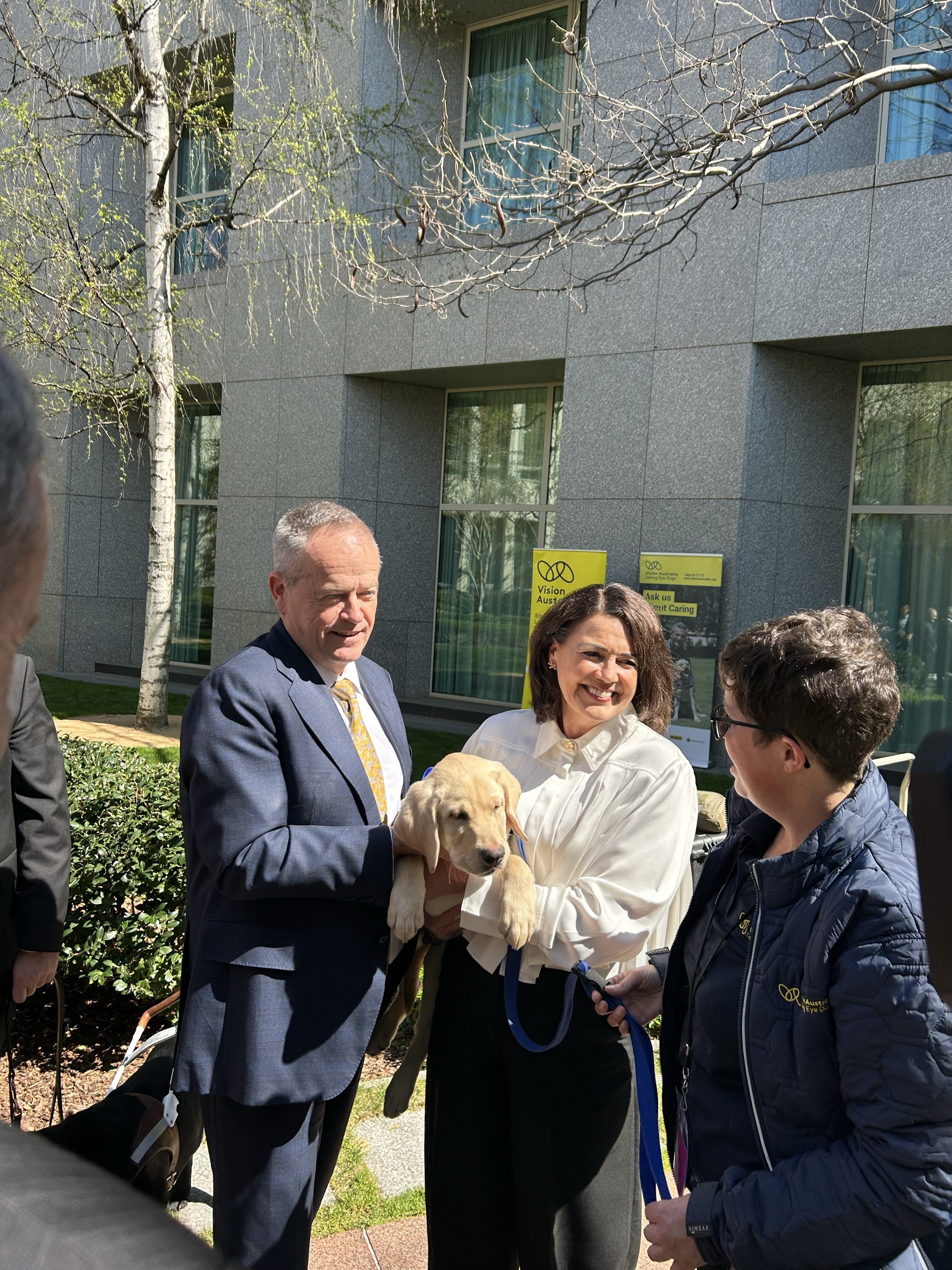 Libby Coker MP holding a yellow Seeing Eye Dogs puppy while talking to one of our staff members, Bill Shorten MP is next to Libby.