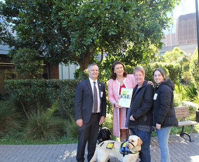 Three women, one with a seeing eye dog, and man stand in a garden area
