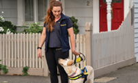 Seeing Eye Dogs instructor Jacqui looks down and smiles at yellow Seeing Eye Dog Tambo